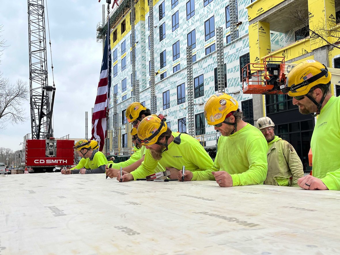 CD Smith Construction crew signs last piece of CLT for topping off Bakers Place mass timber building crane and USA flag in background in Madison Wisconsin