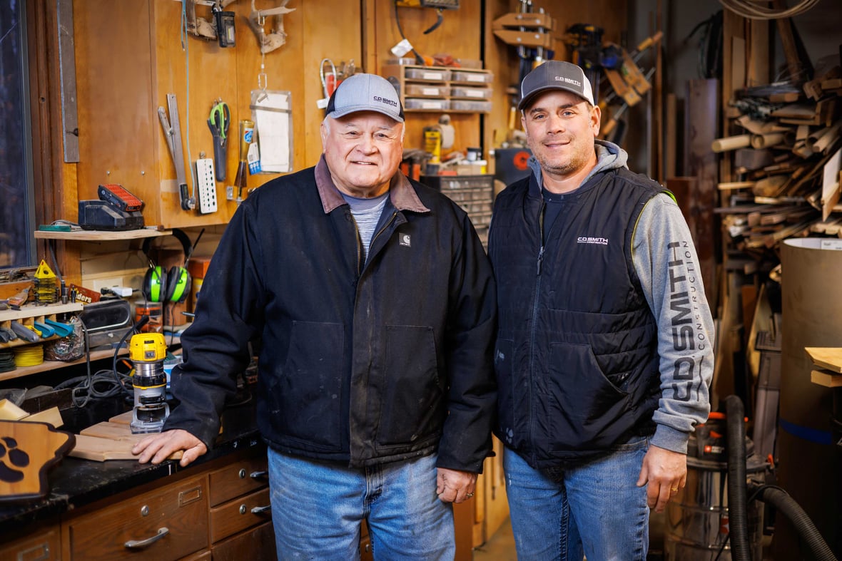 CD Smith Superintendent Steve Julka with retired father Arlyn posed together in a workshop wearing branded clothing