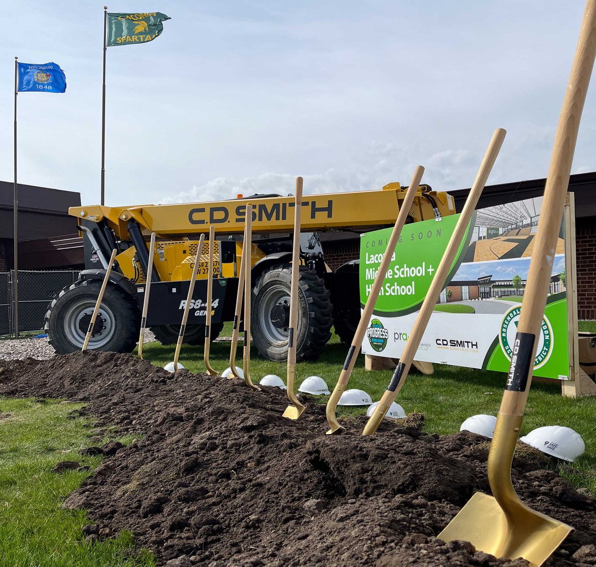 Shovels with project sign and CD Smith Construction equipment in front of Laconia High School for Rosendale Brandon School District groundbreaking ceremony