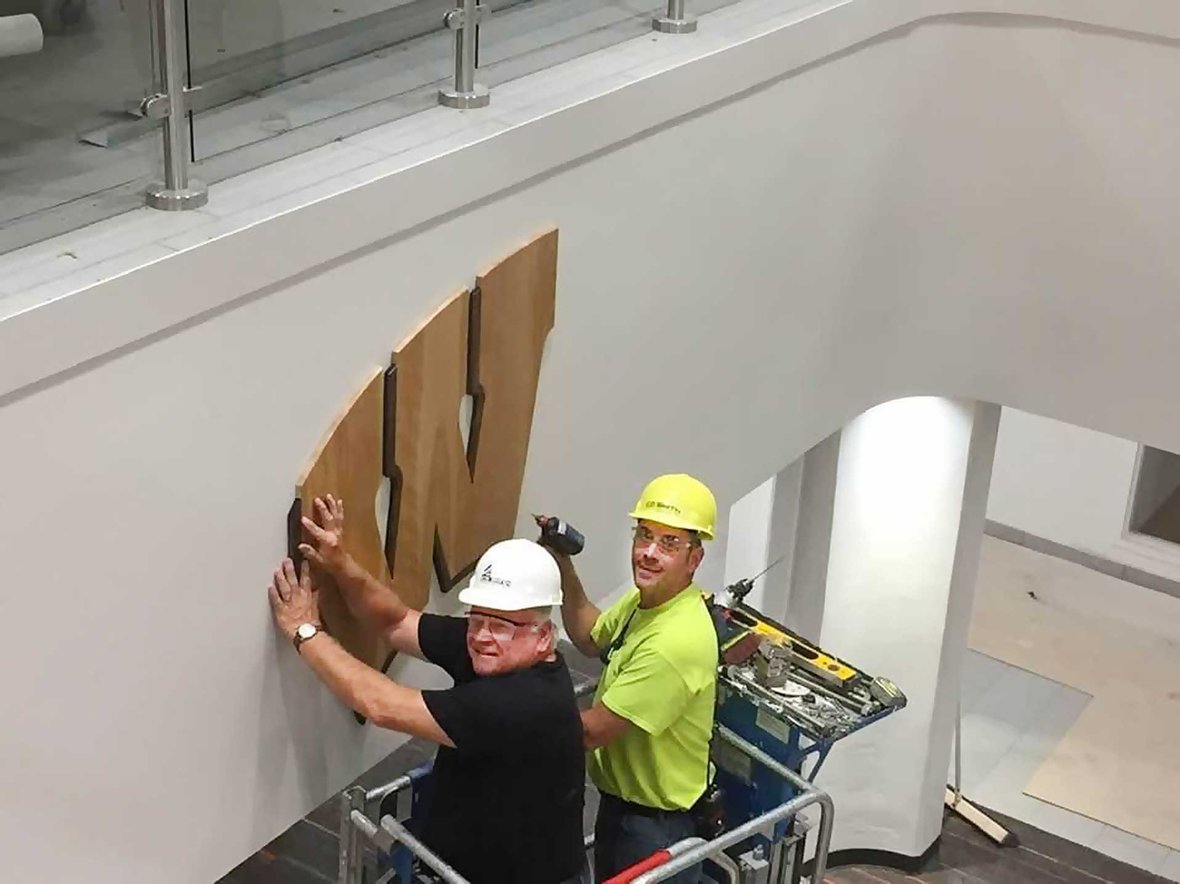 CD Smith Construction Superintedent Steve Julka and retired superintendent Arlyn Julka on a lift installing UW-Madison Badger logo in a residence hall