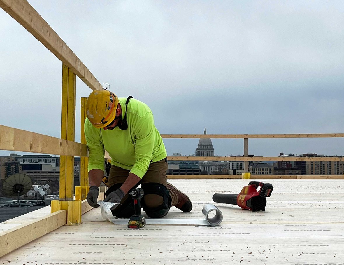 CD Smith Construction carpenter working on top floor of Bakers Place mass timber building with capital building in background in Madison Wisconsin