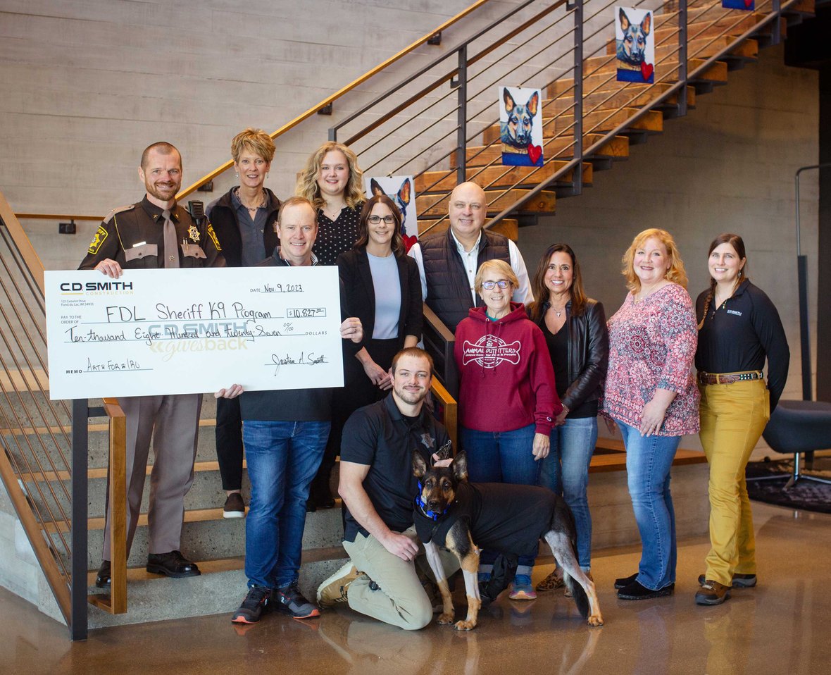 Group of Donors and Recipients with giant check to FDL Sheriff K9 Porgram on steps at CD Smith Construction Fond du Lac WI Office