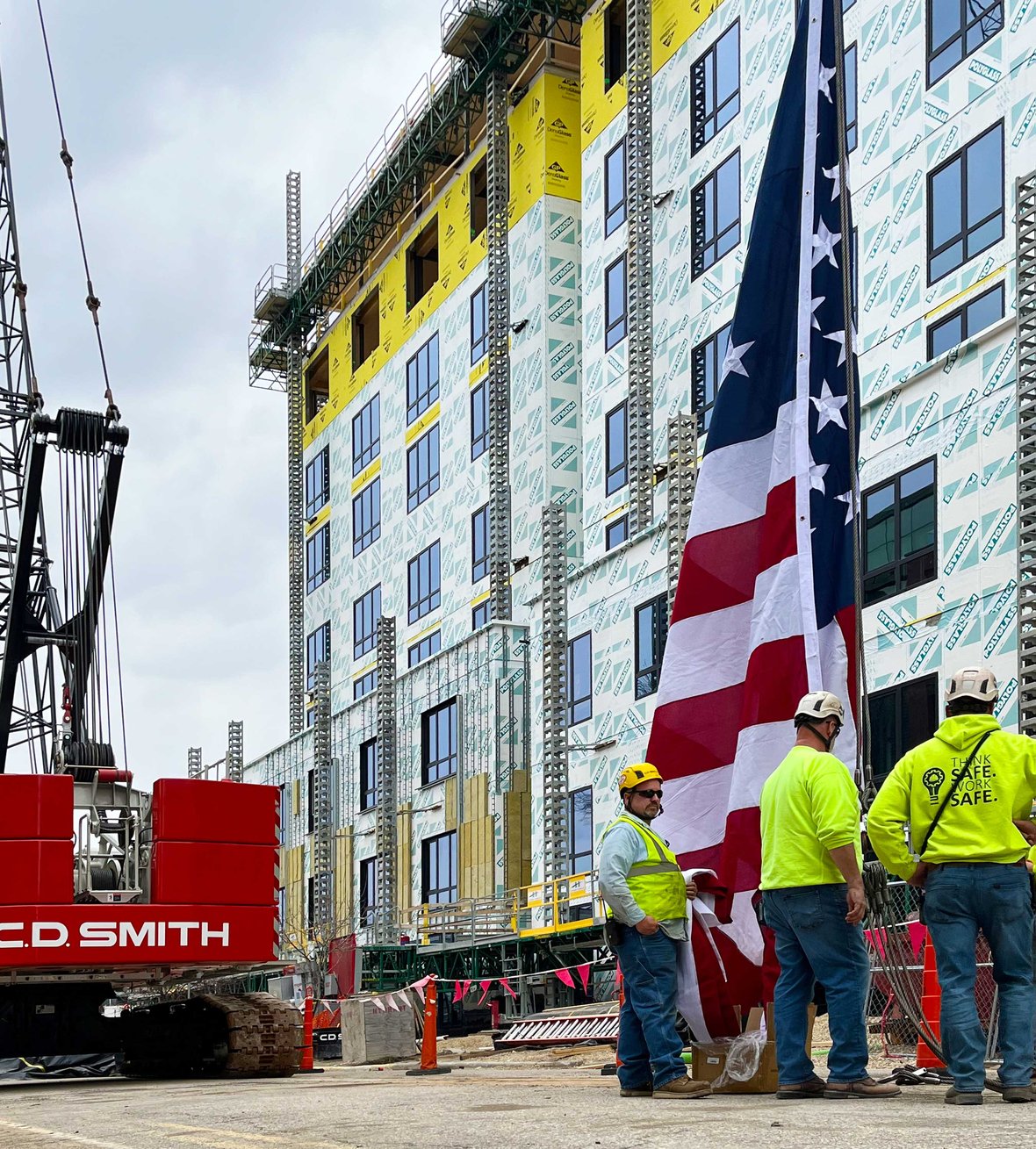 CD Smith Construction team with large USA flag attached to crane at Bakers Place mass timber building in Madison Wisconsin