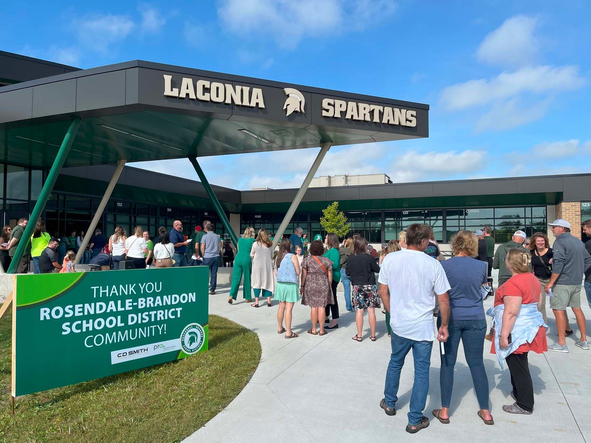 Families and community members gather outside the Laconia school entrance under the canopy with a thank-you sign during the ribbon cutting.