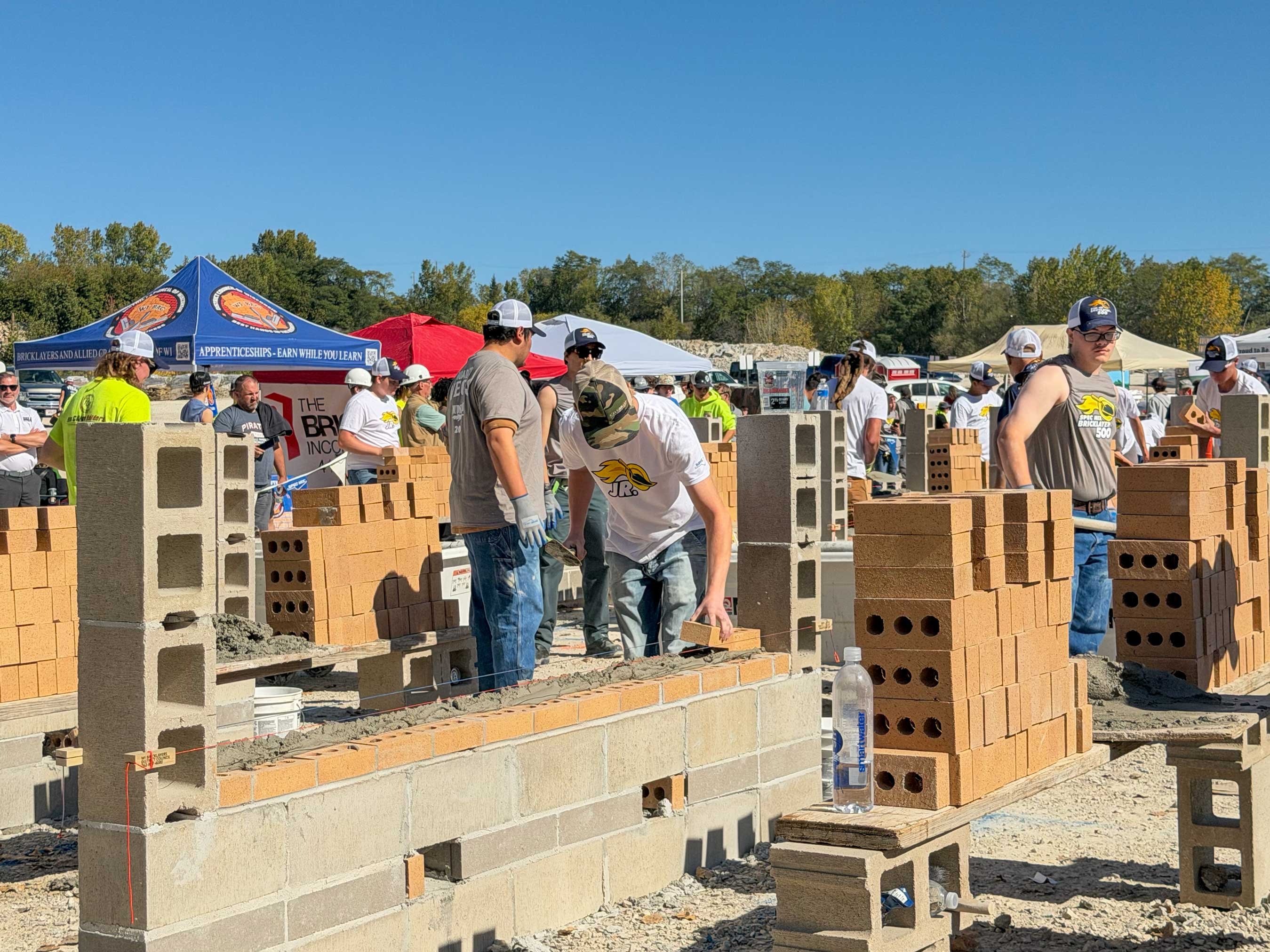 Participants lay brick at the 2026 JR. SPEC MIX Bricklayer 500, with Bricklayers and Allied Craftworkers apprenticeship information nearby.