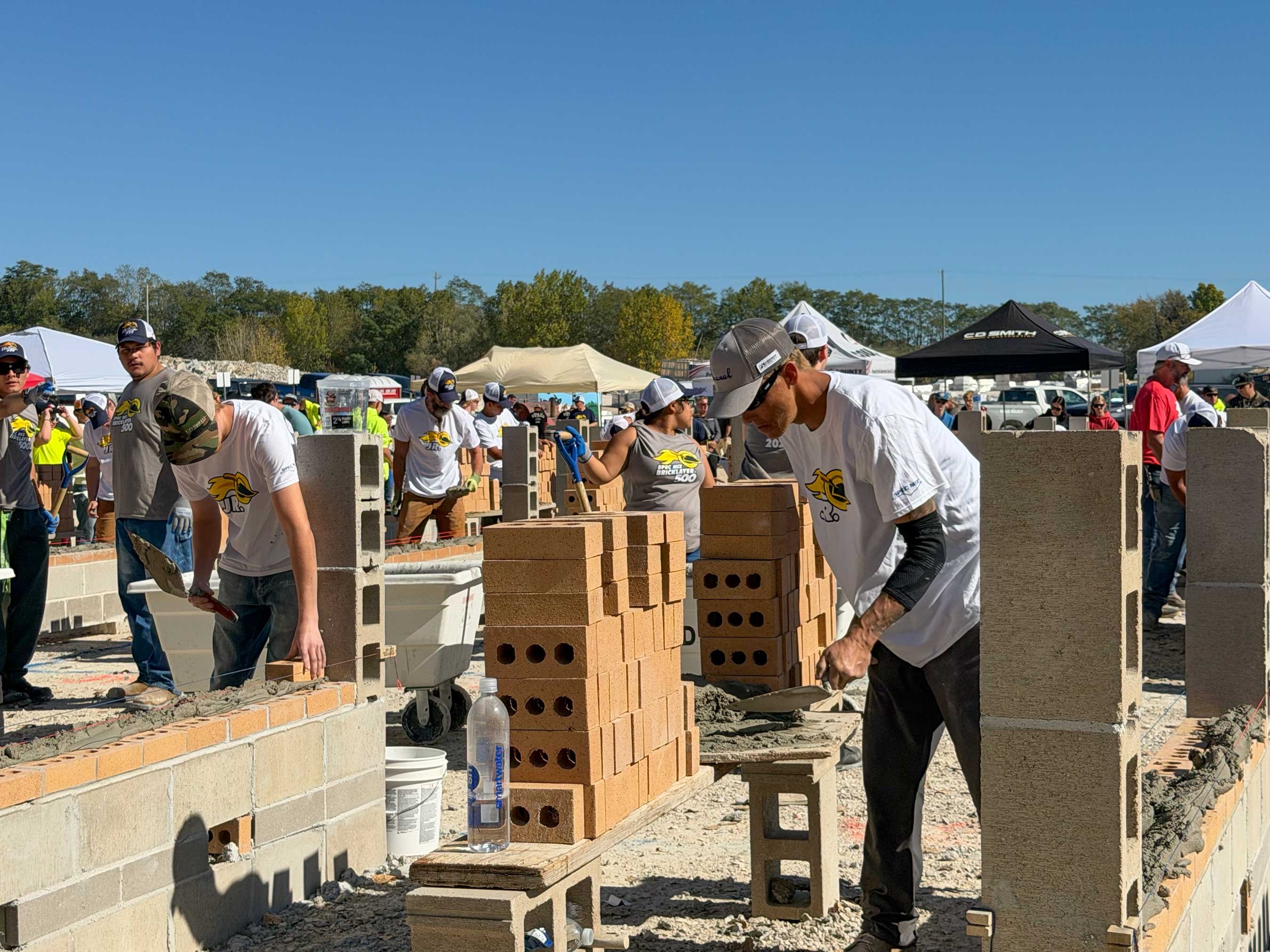 Participants lay brick during the 2026 JR. SPEC MIX Bricklayer 500 Wisconsin Regional in Fond du Lac, with a C.D. Smith tent in the background.