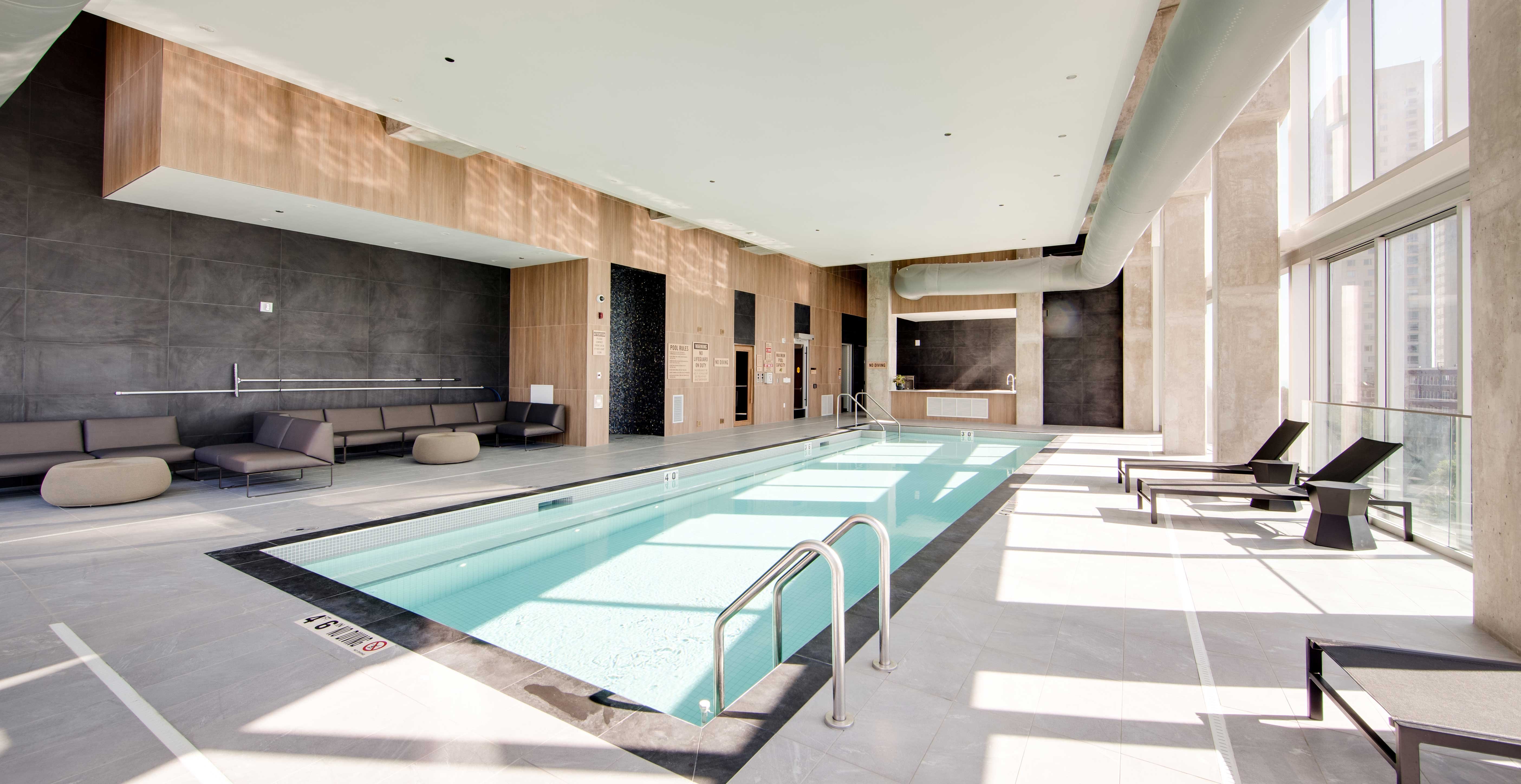 Indoor pool at Ascent Milwaukee with floor to ceiling windows, exposed structural timber, and modern lounge seating.