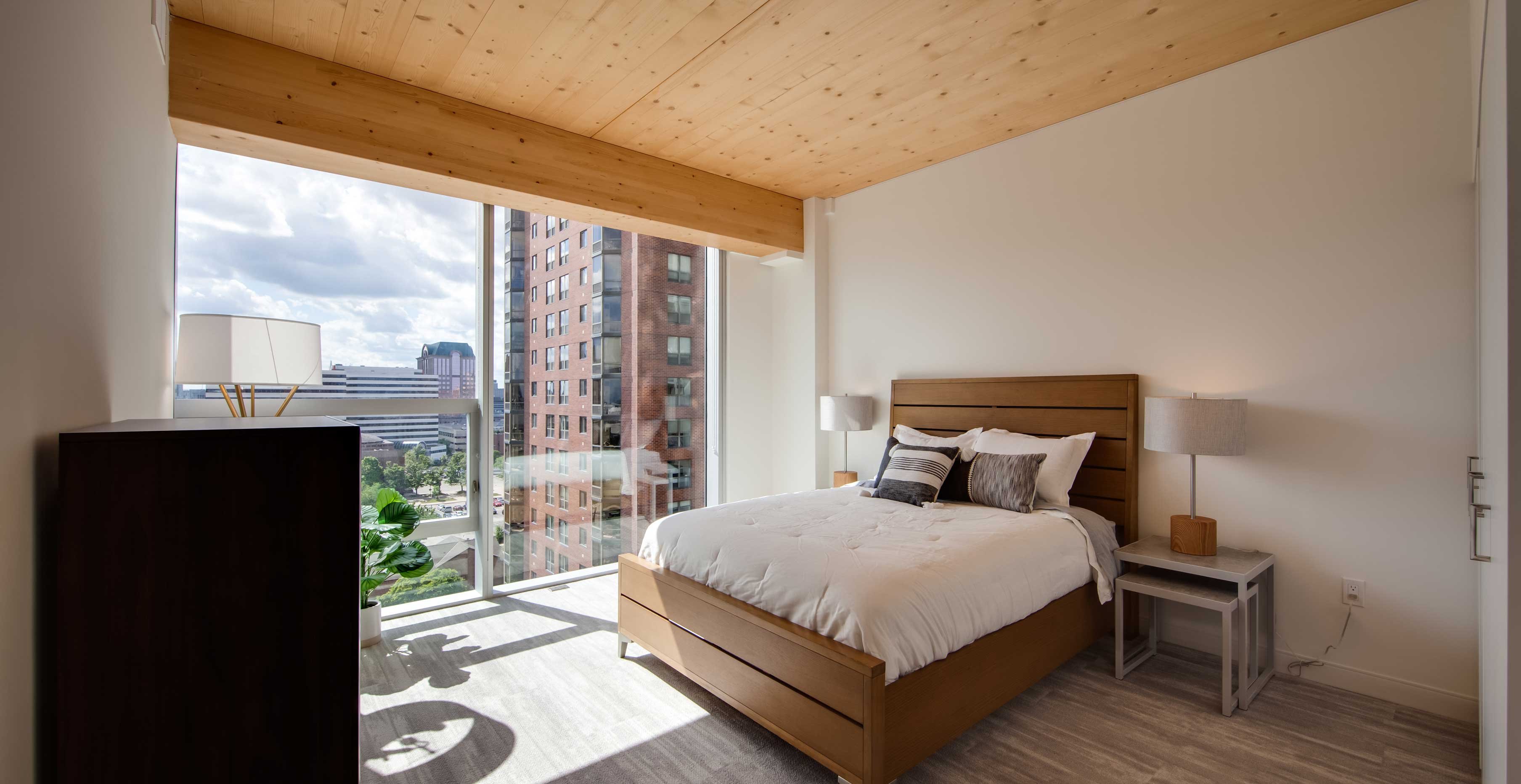 Bedroom interior at Ascent in Milwaukee with exposed mass timber ceiling and floor to ceiling windows overlooking downtown.