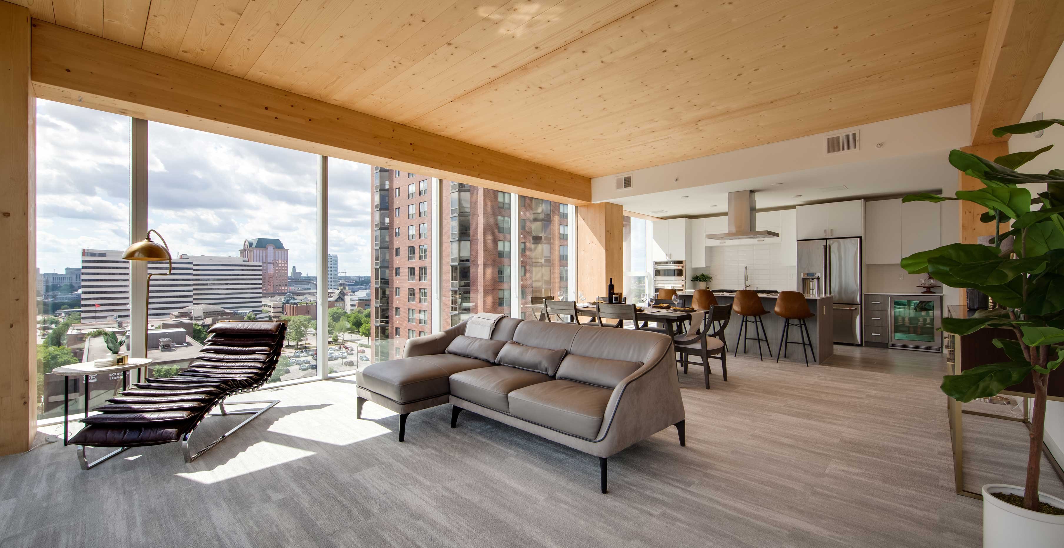 Luxury apartment living room at Ascent in Milwaukee showcasing exposed mass timber ceiling, floor to ceiling windows, and city skyline views.