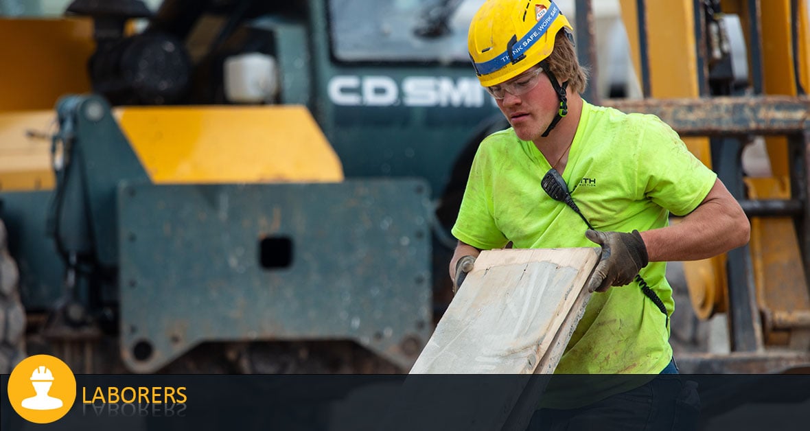 CD Smith Construction Laborer moving lumber on Wisconsin building project jobsite with equipment in background