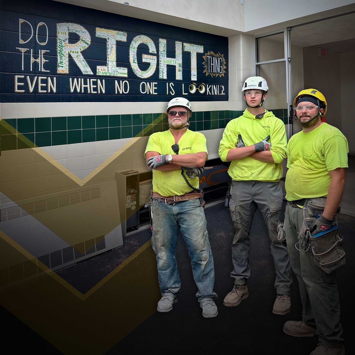 Construction workers standing in front of a Freedom High School wall mural that reads "Do the right thing even when no one is looking" during renovation and facility improvement project by C.D. Smith Construction.