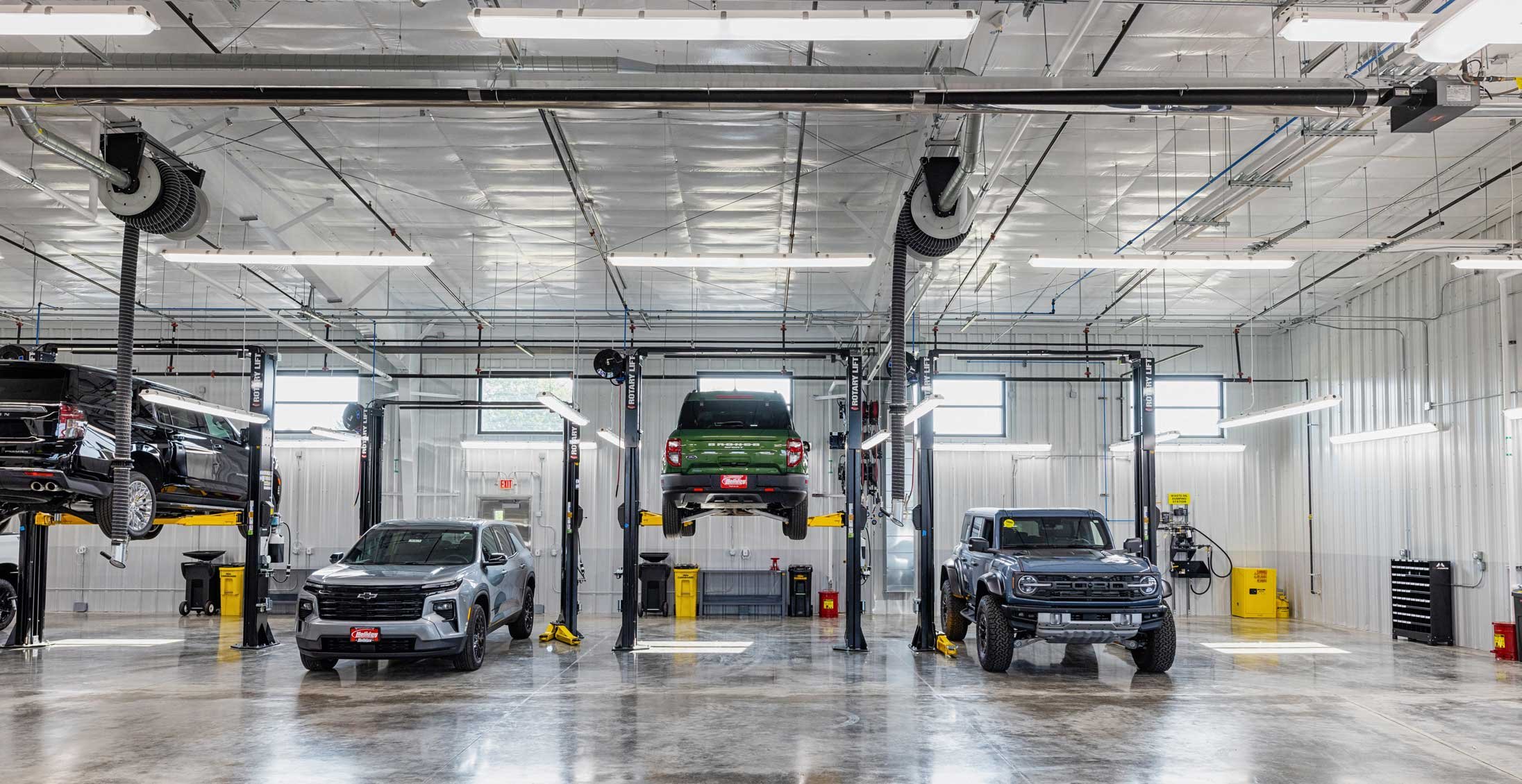 Holiday Automotive Reconditioning Tech Center service bay with multiple vehicles on hydraulic lifts in a high-bay automotive service facility constructed by C.D. Smith.