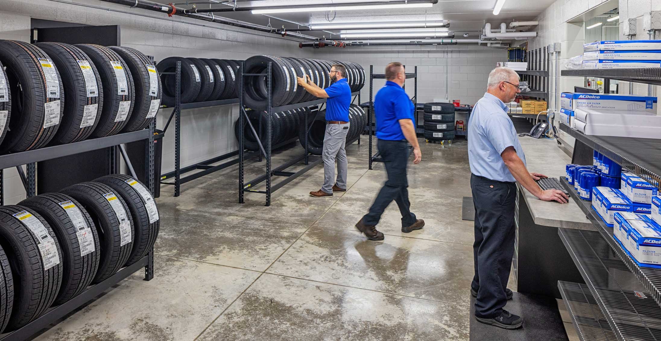 Tire storage and parts distribution area at Holiday Automotive Reconditioning Tech Center featuring organized inventory racking and service counter workspace.
