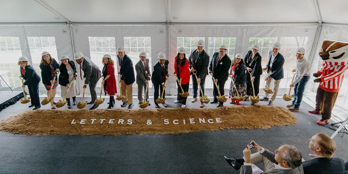 Stakeholders hold shovels with dirt at groundbreaking event of UW-Madison Levy Hall with Bucky Badger