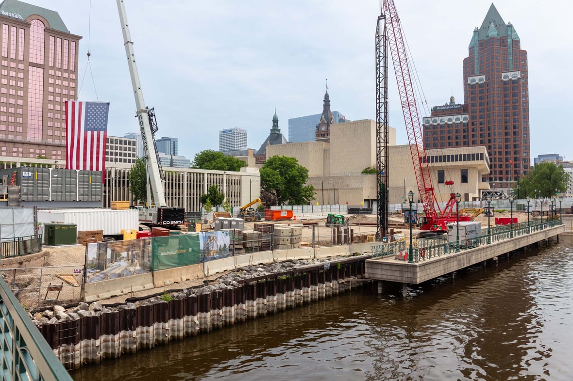 Neutral Edison mass timber construction site with CD Smith cranes and flags for groundbreaking view from Milwaukee river