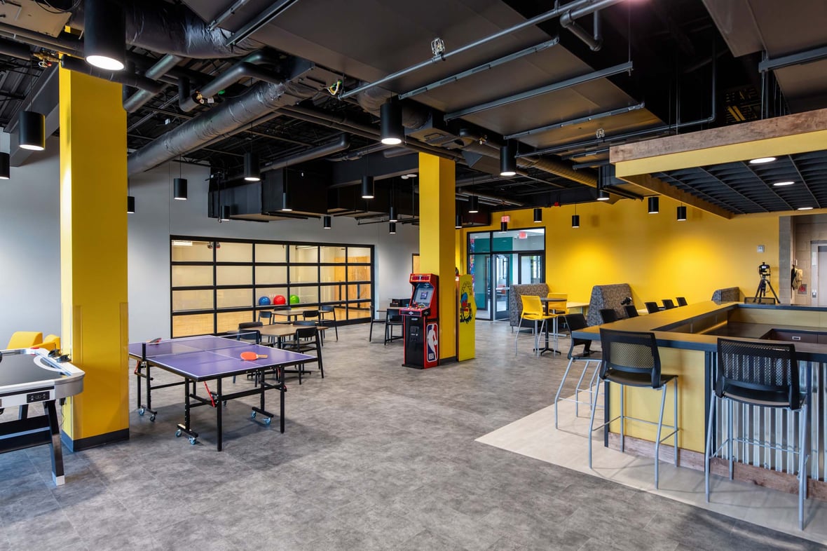 Newly built teen hangout space at the Ripon Boys &amp; Girls Club featuring games, seating, snack area, and a glass garage door leading to the dance and recording studios—part of a youth-focused facility delivered through commercial construction services in Wisconsin.