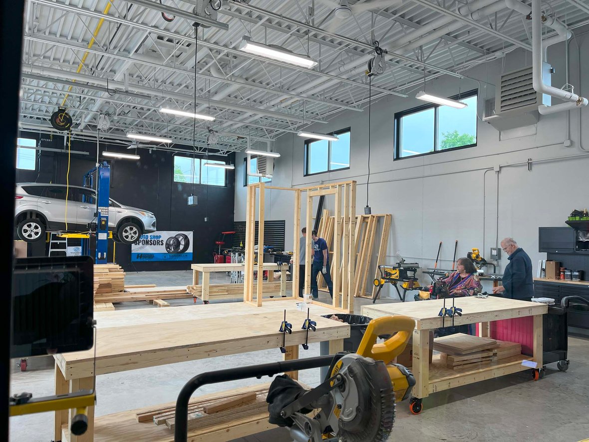 Ribbon cutting guests tour the Ripon Boys &amp; Girls Club’s tech ed area, featuring a car on a hoist and wood framing construction—part of a youth-focused facility built through commercial construction services in Wisconsin to support hands-on learning and skilled trades exploration.