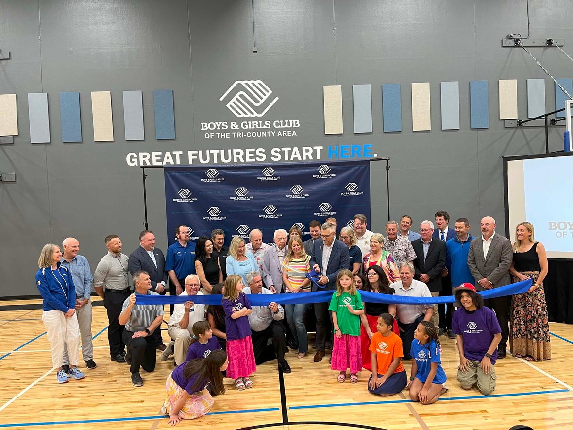 Jason Presto prepares to cut the ribbon with oversized scissors alongside donors and community leaders inside the Ripon Boys &amp; Girls Club gym—celebrating the grand opening of a youth-focused facility built through commercial construction services in Wisconsin.