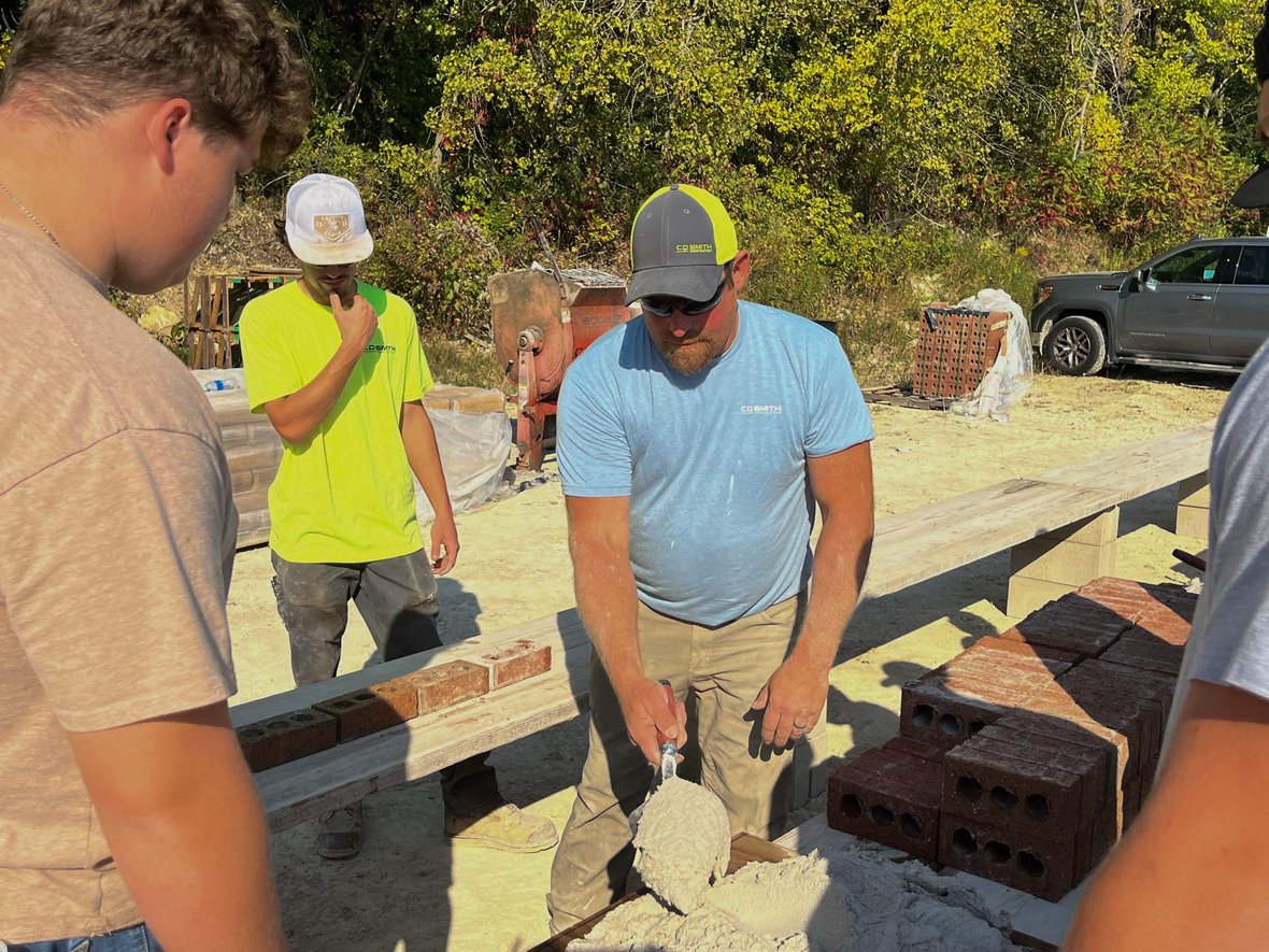 Mason shows students how to butter bricks with mortar at the 2025 Bricklayer 500.