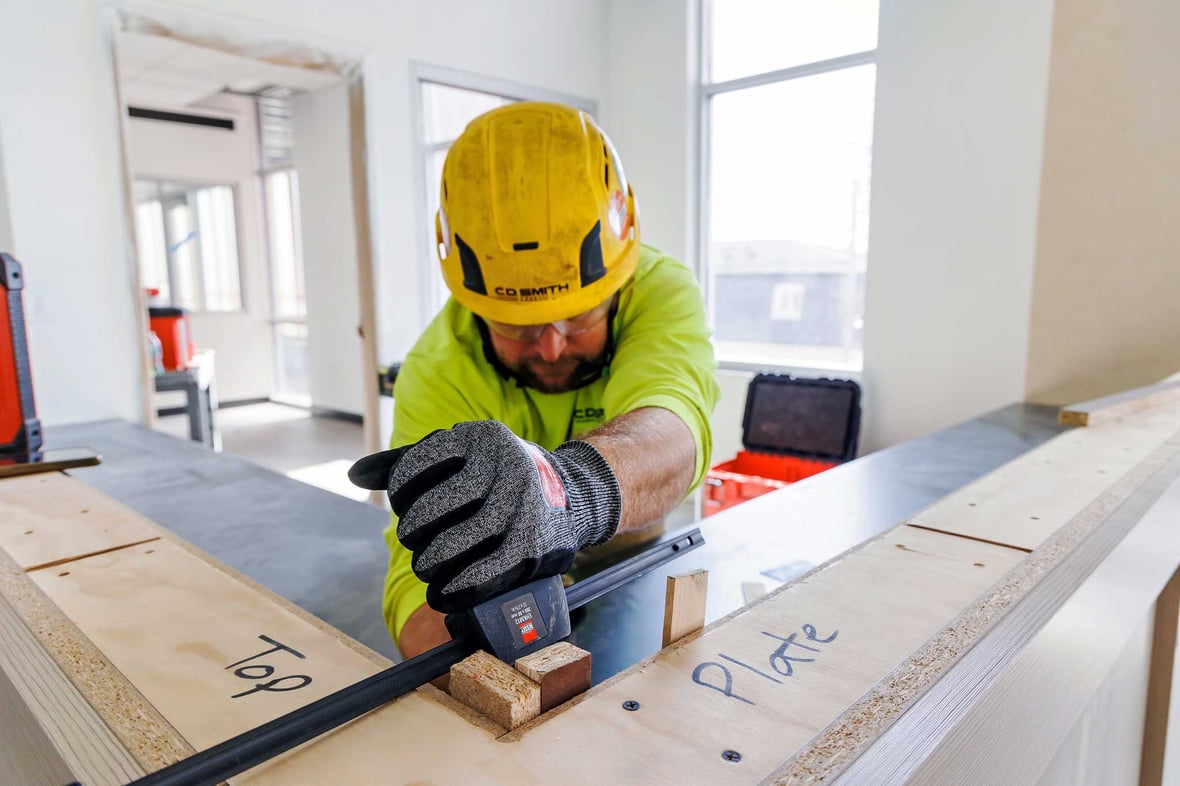 C.D. Smith carpenter measuring and securing interior framing components; ProjectPlus team craftsmanship shown during detailed construction work.