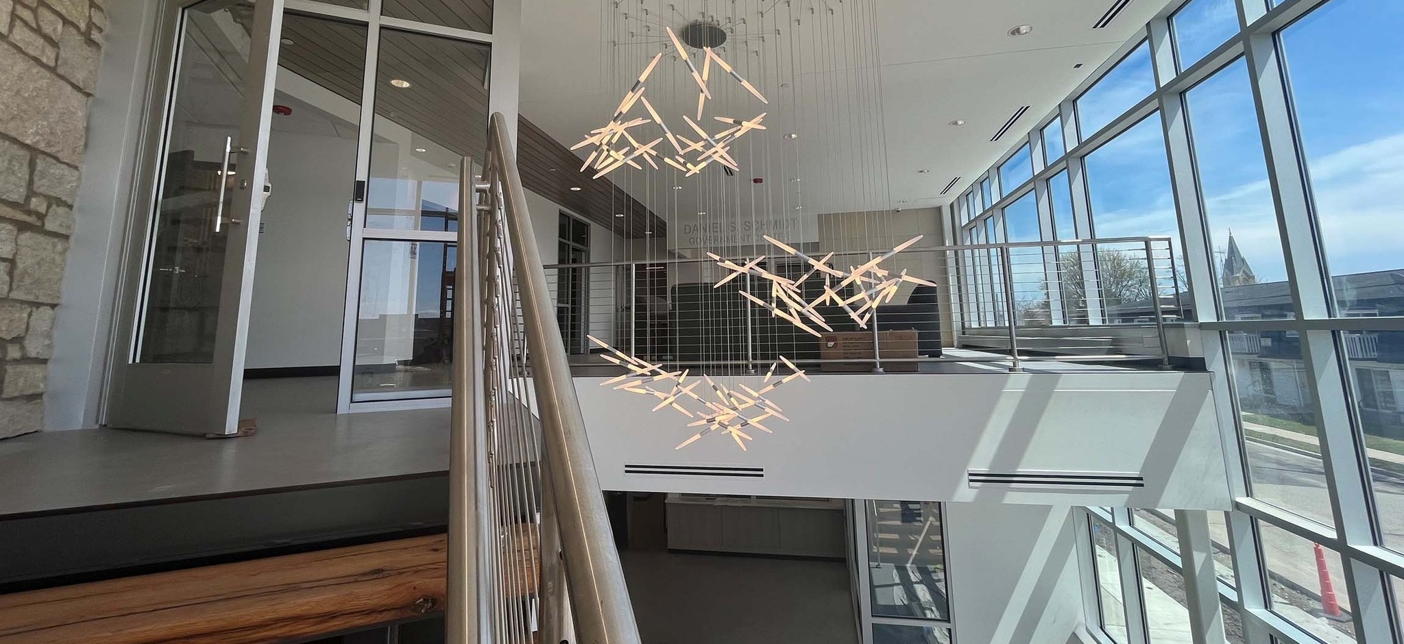 Interior view of the Kewaskum Community Center featuring modern staircase, stone accent wall, and contemporary light fixture in the two-story atrium. Designed and built by C.D. Smith Construction.