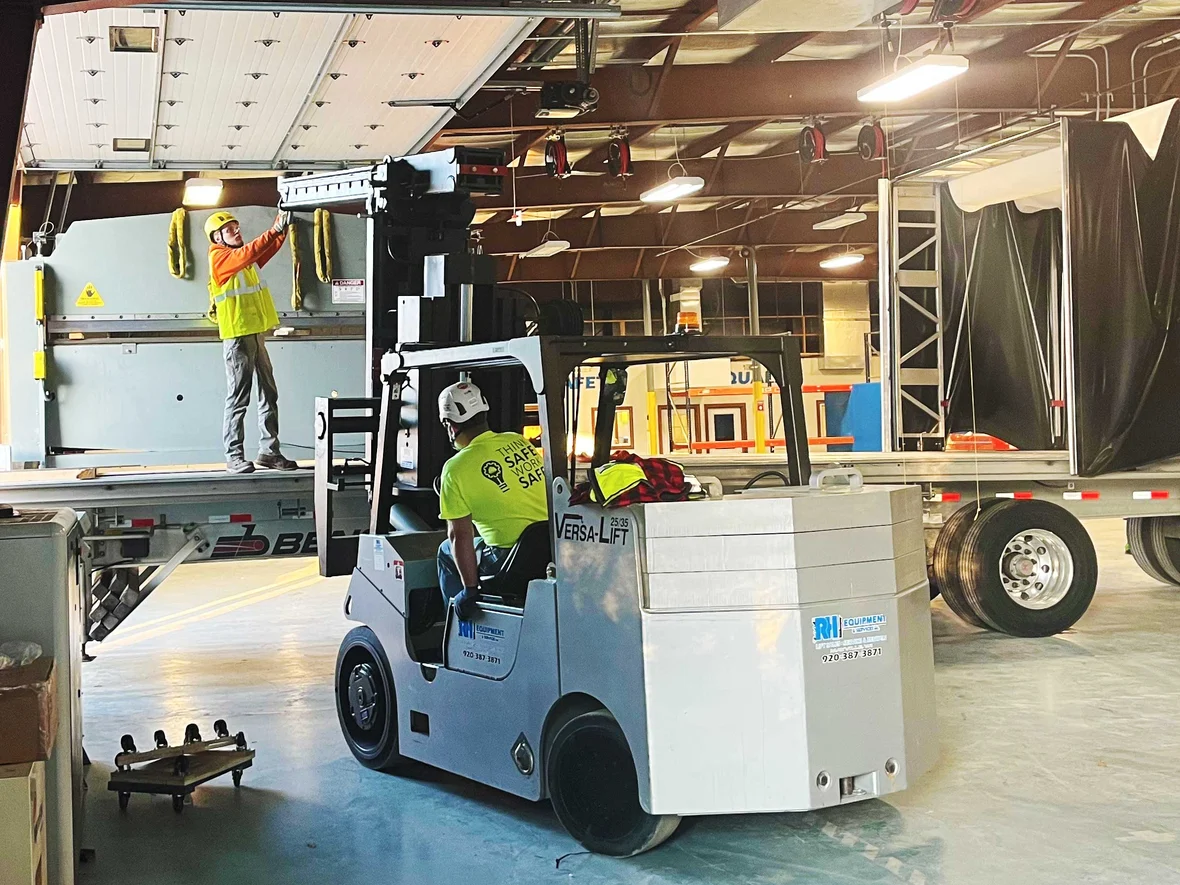 Millwrights operating a Versa Lift to position a 10,000-pound shearing machine inside an active industrial facility.