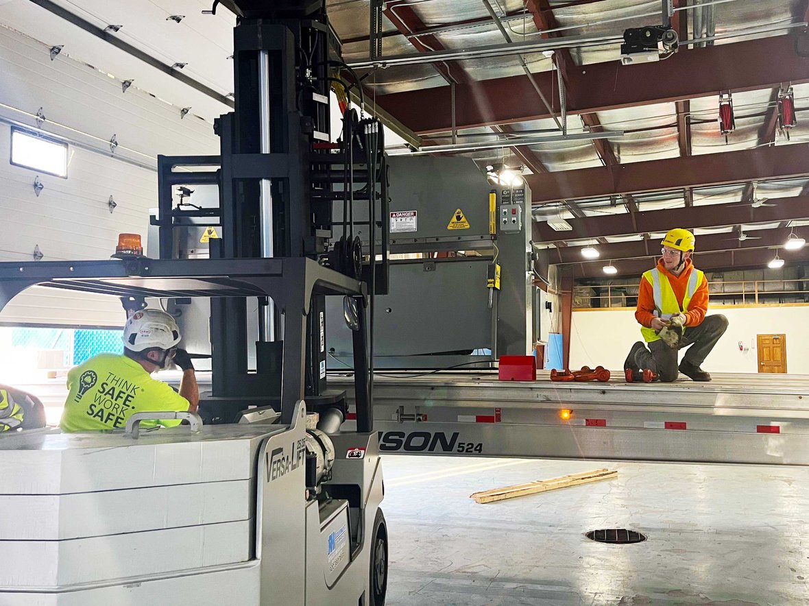 Millwrights using forklifts to lift and position a 10,000-pound shearing machine inside an active facility.