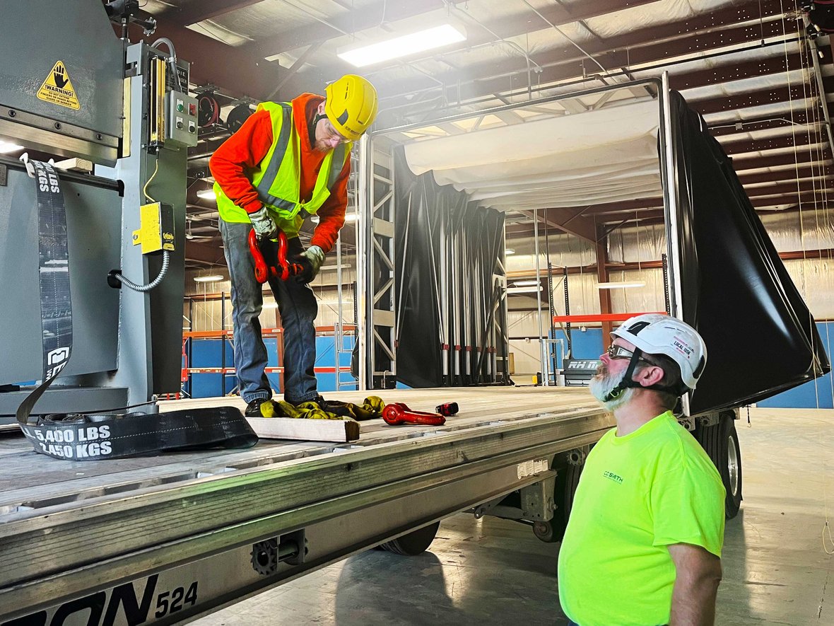 Millwright coordinating with a teammate during shearing machine relocation, confirming rigging alignment and safety checks.