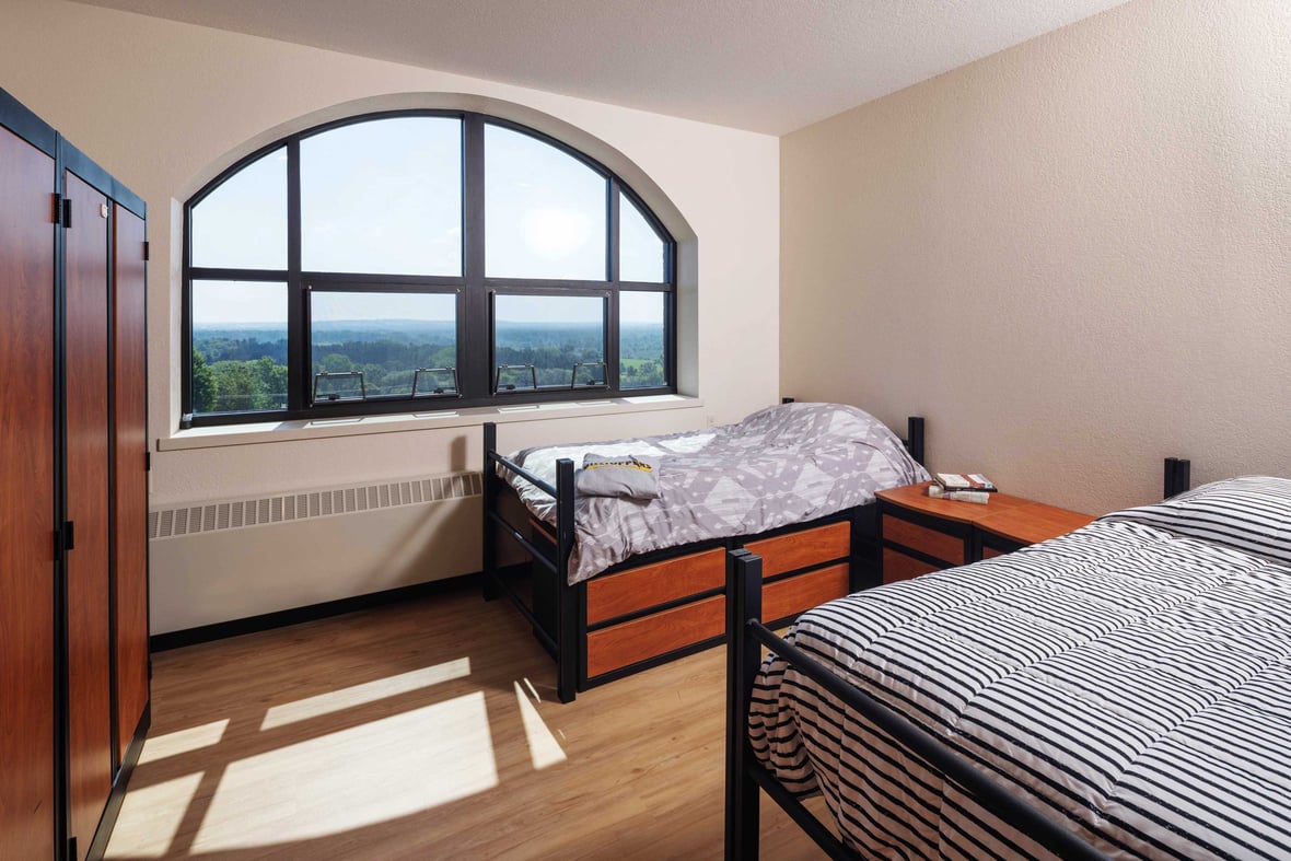 Student dorm room in Fr. Solanus Hall at St. Lawrence Seminary with beds, built in storage and large arched window