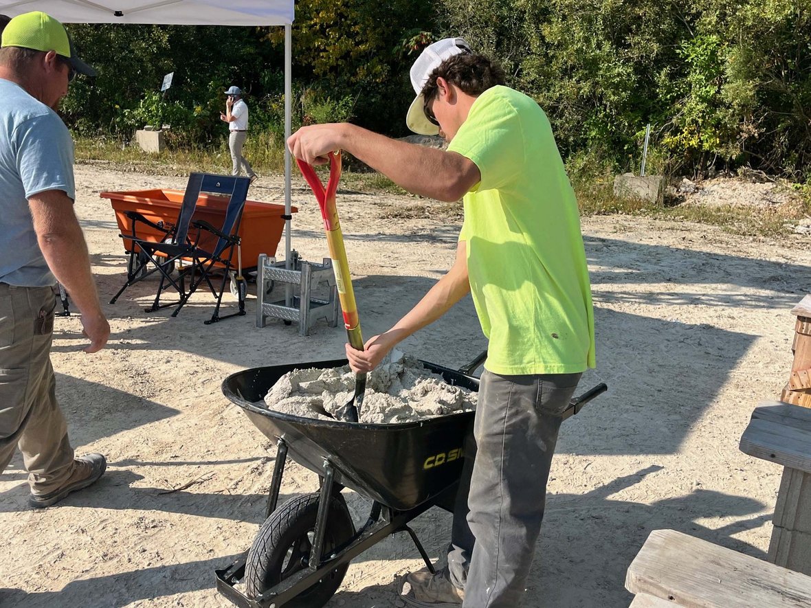 Student mixes mortar in a wheelbarrow under supervision at the 2025 Spec Mix Bricklayer 500.