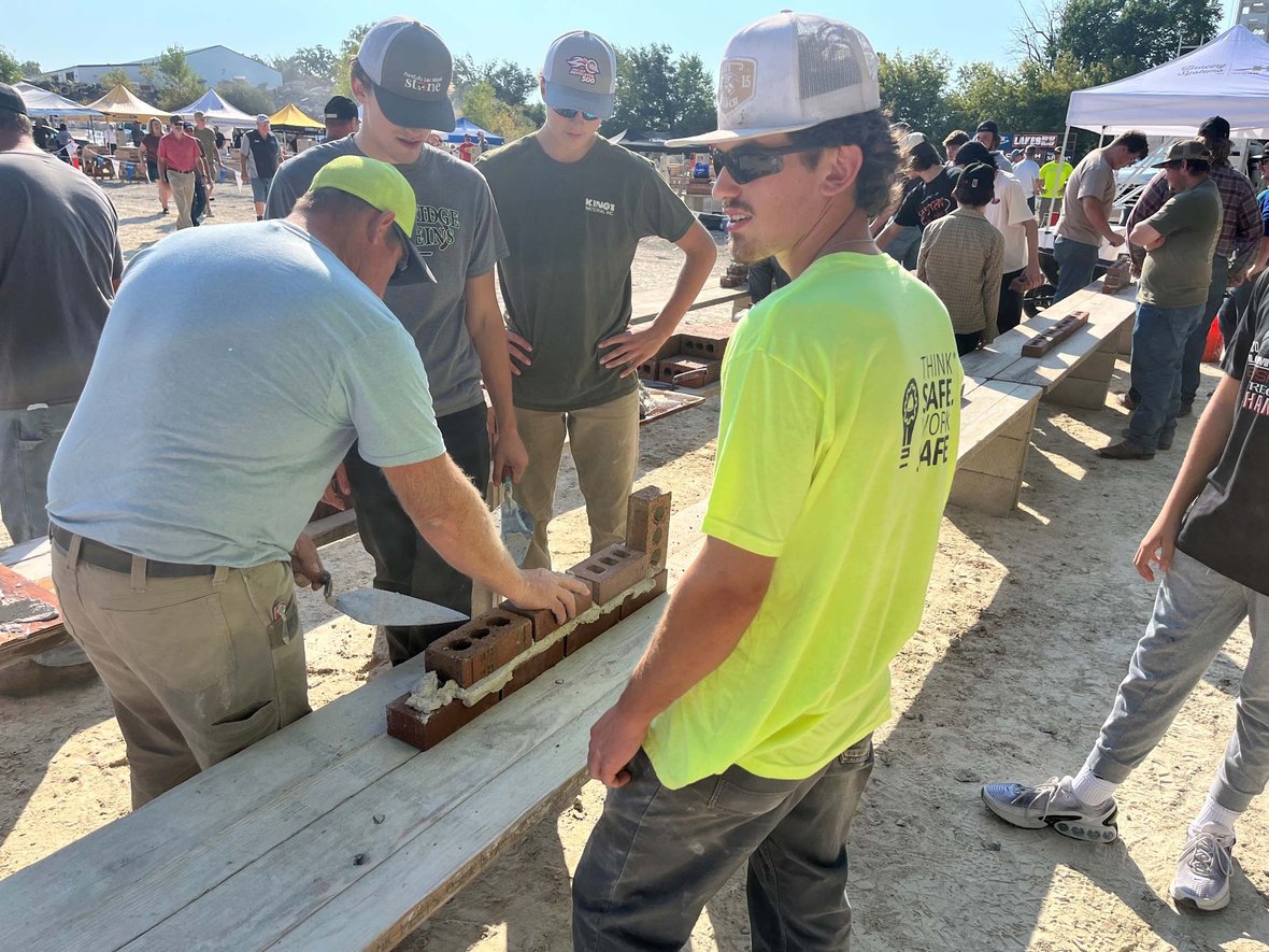 High school students practice laying bricks with guidance at the ACE Academy station during the 2025 Bricklayer 500.
