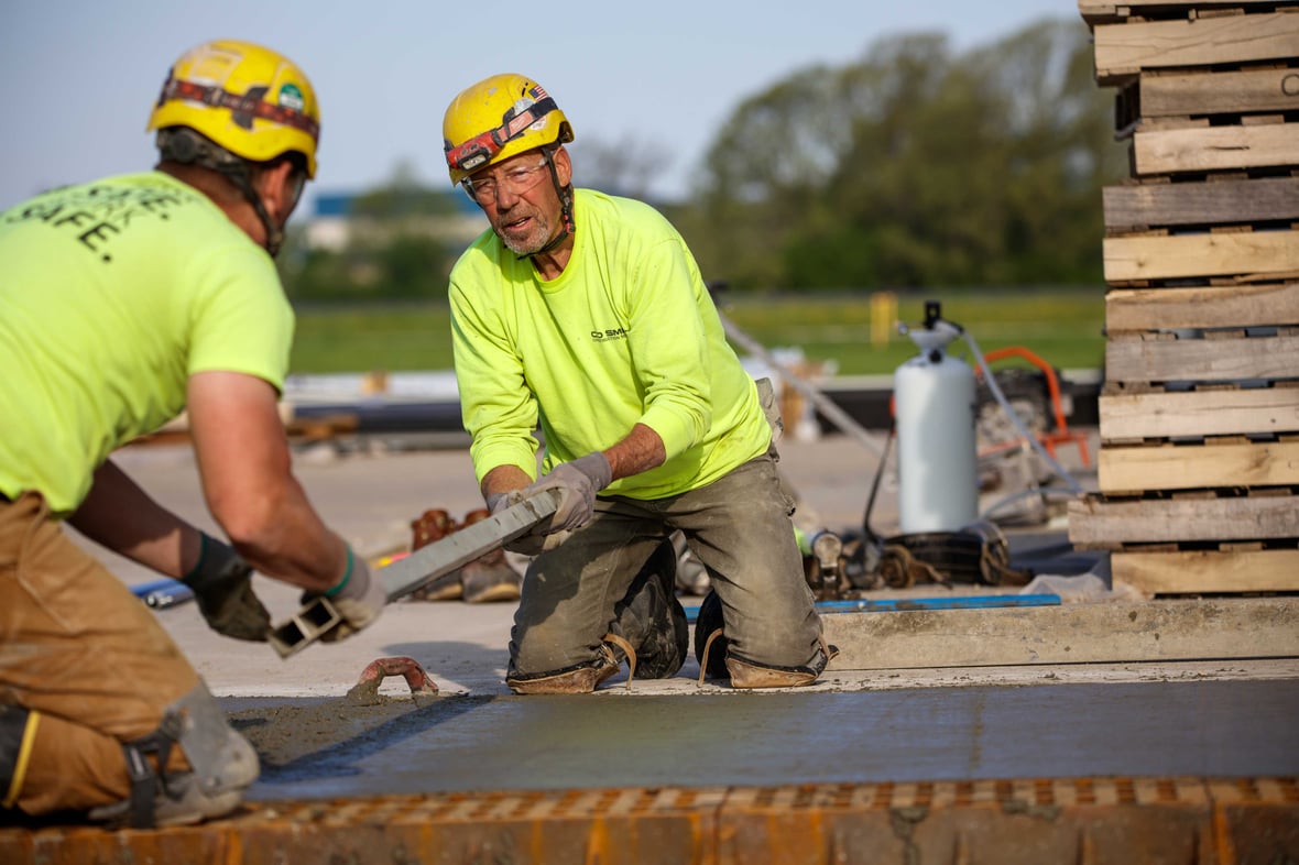 Construction workers in safety gear pouring and leveling concrete on a commercial job site in Wisconsin, demonstrating proper PPE use with helmets, gloves, and high-visibility clothing.